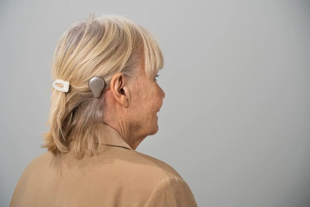 An older woman seen from behind, wearing a small bone conduction processor on the skull just behind her ear.